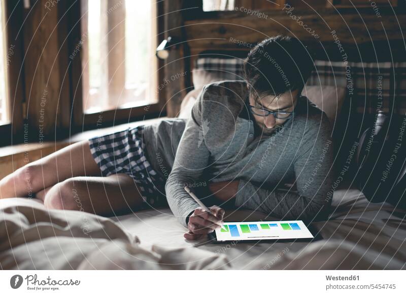 Junger Mann liegt im Bett und analysiert Daten auf Tablette Tablet Computer Tablet-PC Tablet PC iPad Tablet-Computer Männer männlich Betten Rechner Erwachsener