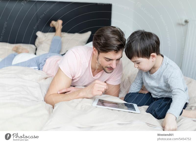 Vater und Sohn betrachten die Tablette im Bett Betten Söhne Tablet Computer Tablet-PC Tablet PC iPad Tablet-Computer Papas Väter Vati Vatis Papis Kind Kinder