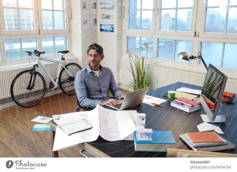 Mann mit Laptop am Schreibtisch im Büro Office Büros Männer männlich Geschäftsmann Businessmann Businessmänner Geschäftsmänner Notebook Laptops Notebooks