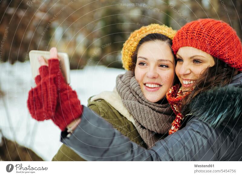 Zwei Freunde machen Selfies im Schnee Freundinnen Freundschaft Kameradschaft Winter winterlich Winterzeit Smartphone iPhone Smartphones lachen fotografieren