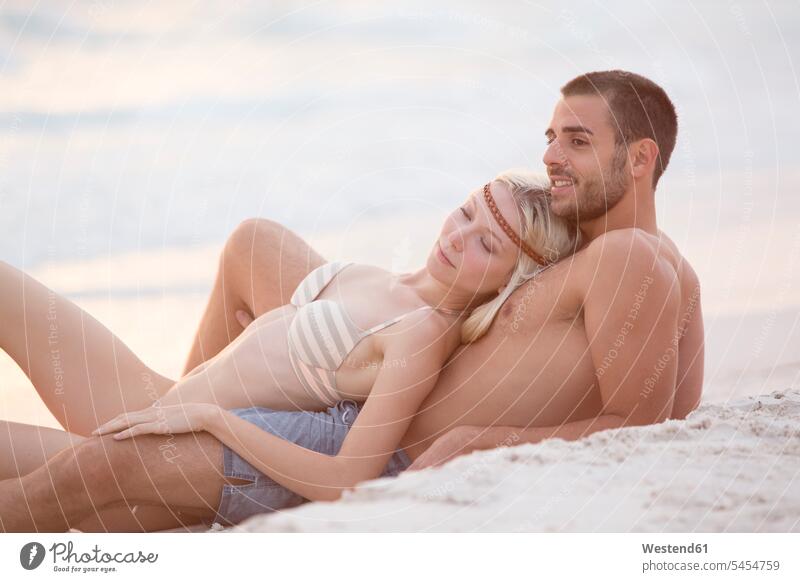 Junges Paar sitzt am Strand und umarmt Erotik Sexualität verliebt romantisch schwärmerisch schwaermerisch gefuehlvoll gefühlvoll Romantik Beach Straende Strände