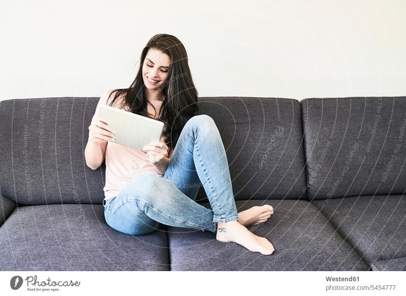 Lächelnde junge Frau sitzt mit Tablette auf Couch entspannt entspanntheit relaxt Tablet Computer Tablet-PC Tablet PC iPad Tablet-Computer lächeln weiblich