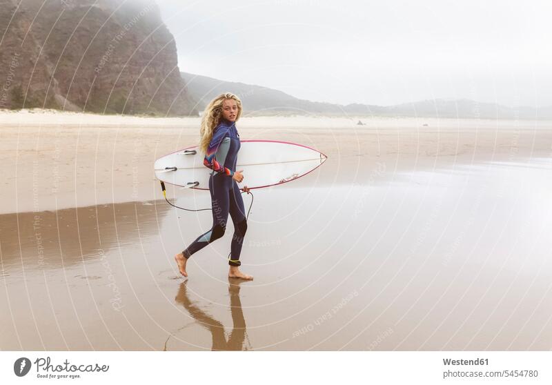 Spanien, Aviles, junger Surfer auf dem Weg zum Wasser Surfbrett Surfbretter surfboard surfboards Teenagerin junges Mädchen Teenagerinnen weiblich junge Frau