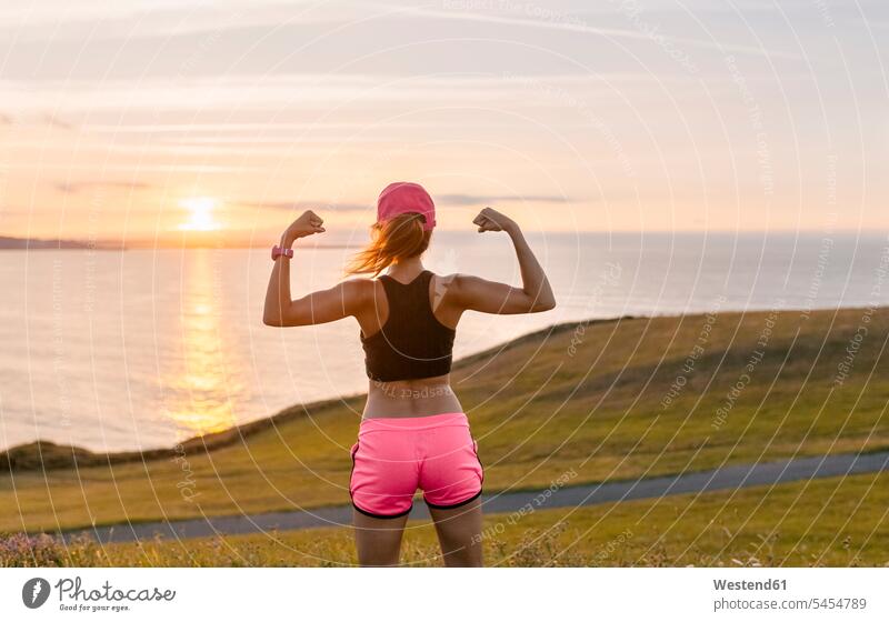 Junge Frau, die nach dem Training auf das Meer schaut und ihre Muskeln beugt trainieren weiblich Frauen Erwachsener erwachsen Mensch Menschen Leute People