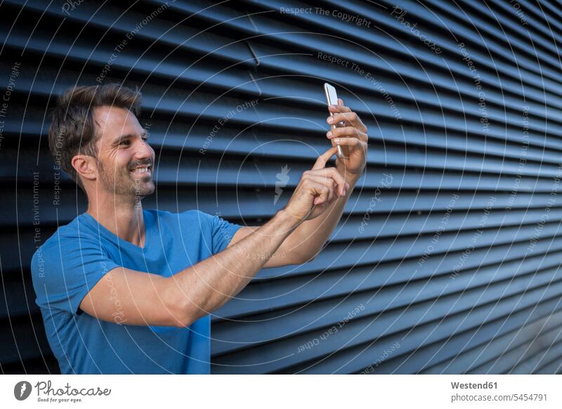 Mann steht vor einem Rolltor und macht ein Selfie Handy Mobiltelefon Handies Handys Mobiltelefone Zuversicht Zuversichtlich Selbstvertrauen selbstbewusst