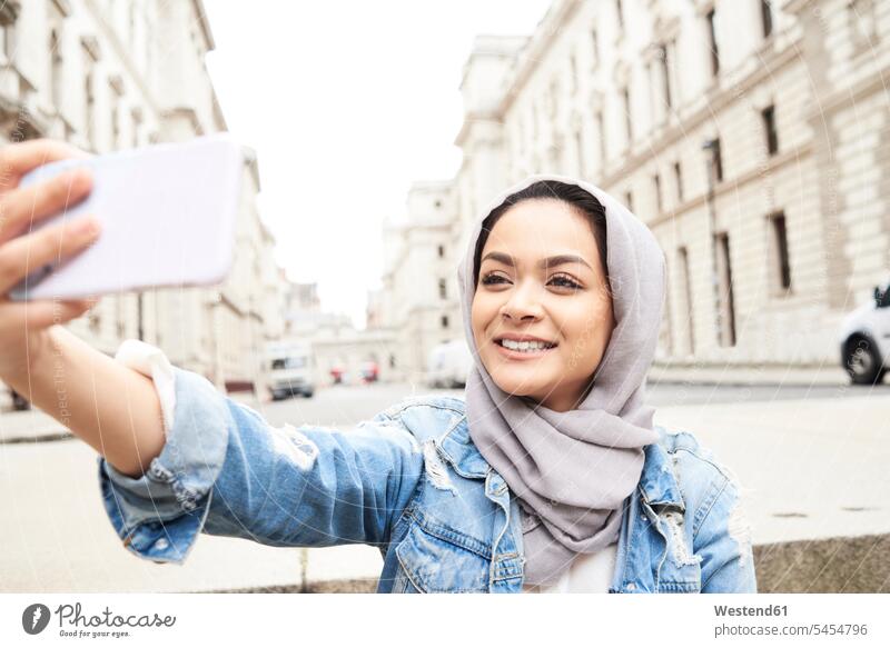 UK, England, London, junge Frau mit Hidschab, die ein Selfie in der Stadt macht Kopftuch Kopftücher muslimisch Moslem Muslim Handy Mobiltelefon Handies Handys