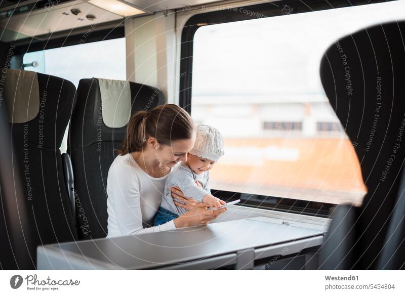 Mutter mit Baby Mädchen reist mit dem Zug und schaut auf Handy reisen verreisen Mami Mutti Mütter Mama Mobiltelefon Handies Handys Mobiltelefone Fenster Babies