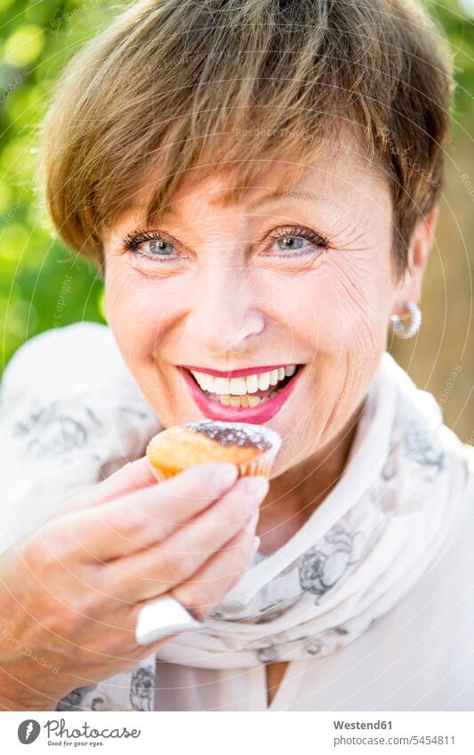 Porträt einer lächelnden älteren Frau, die im Freien einen Muffin isst weiblich Frauen Muffins essen essend Seniorin Seniorinnen alt Erwachsener erwachsen