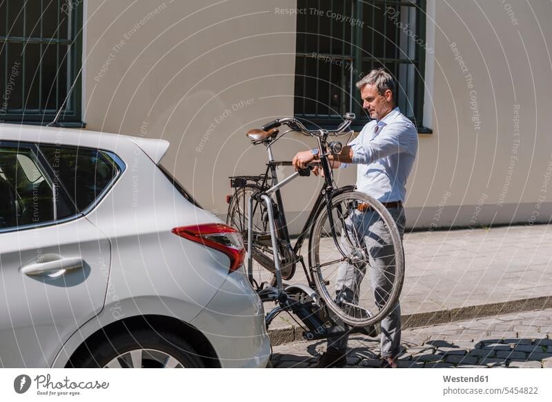 Mann befestigt Fahrrad auf Anhänger am Auto Männer männlich Bikes Fahrräder Räder Rad Wagen PKWs Automobil Autos Stadt staedtisch städtisch Erwachsener