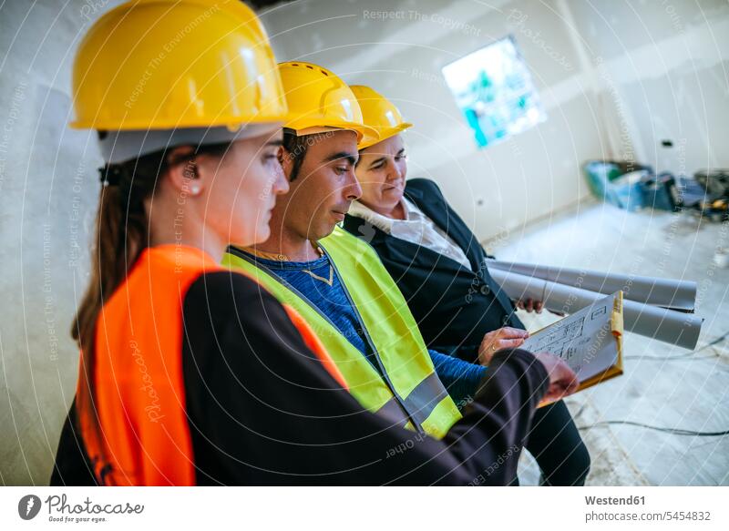 Zwei Frauen und Bauarbeiter auf der Baustelle beim Betrachten des Plans Baustellen Bauplan Architekturplan Bauzeichnung Handwerker Handwerksberuf