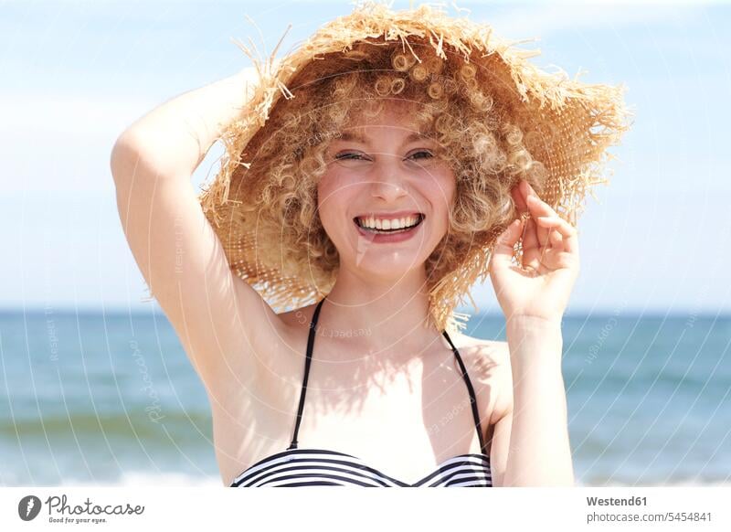 Porträt einer lachenden jungen Frau mit Strohhut am Strand weiblich Frauen Hut Hüte Portrait Porträts Portraits Erwachsener erwachsen Mensch Menschen Leute