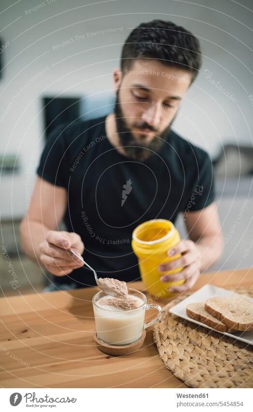 Junger Mann bereitet sein Frühstück zu Hause zu, mischt Kakao und Milch Männer männlich Erwachsener erwachsen Mensch Menschen Leute People Personen frühstücken