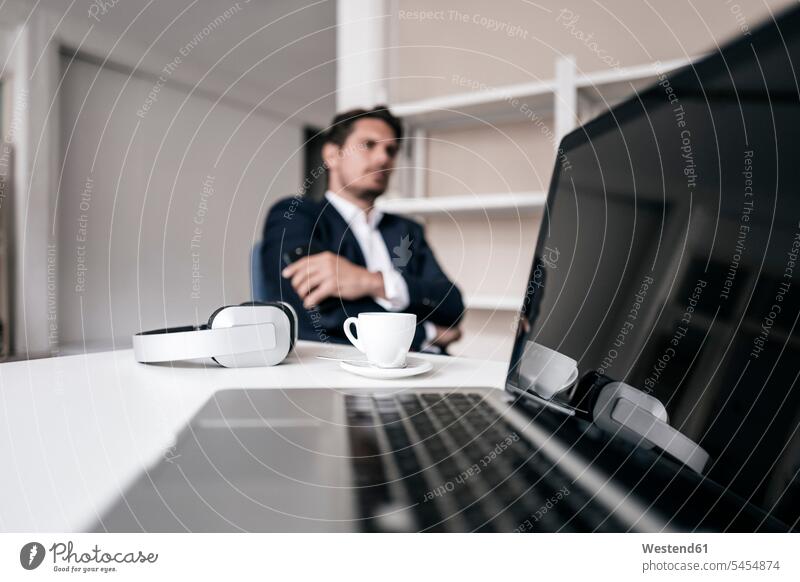 Laptop, Kopfhörer, Kaffeetasse und Geschäftsmann im Hintergrund Kopfhoerer Businessmann Businessmänner Geschäftsmänner Mann Männer männlich Notebook Laptops