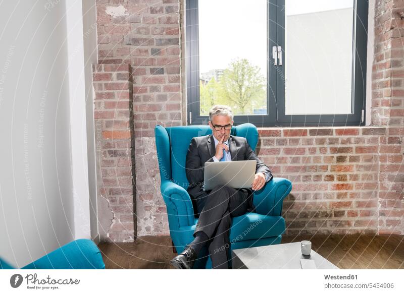 Reifer Geschäftsmann im Sessel sitzend, mit Laptop sitzt Notebook Laptops Notebooks arbeiten Arbeit Fenster Laptop benutzen Laptop benützen nachdenken überlegen