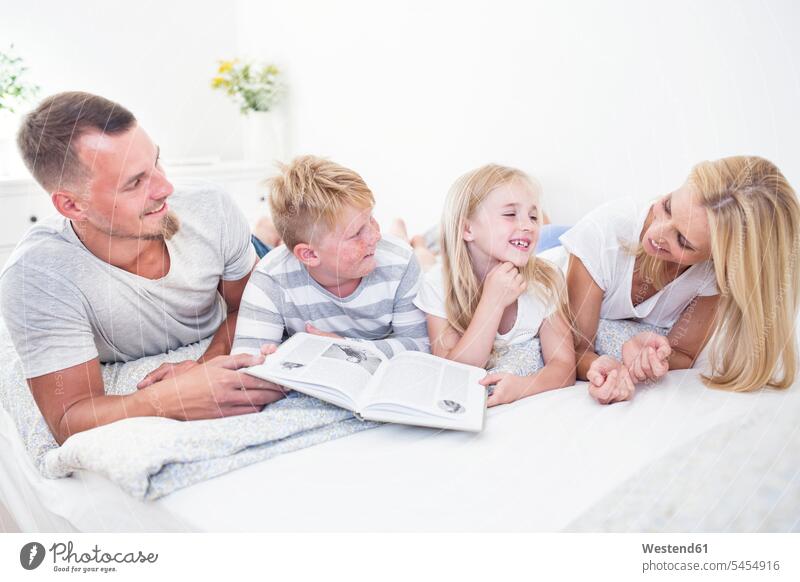 Familie liegt im Bett und liest gemeinsam ein Buch lächeln lesen Lektüre Familien Bücher Betten Mensch Menschen Leute People Personen Zuhause zu Hause daheim
