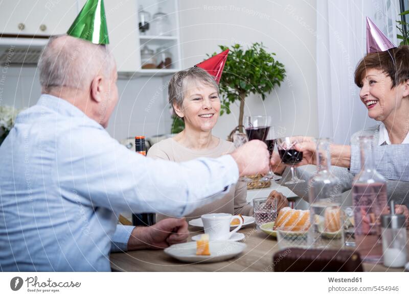 Zwei ältere Paare feiern Geburtstag und stoßen mit Rotwein an anstoßen zuprosten anstossen Rotweine trinken Geburtstagsfeiern Geburtstage Partyhut Papphut
