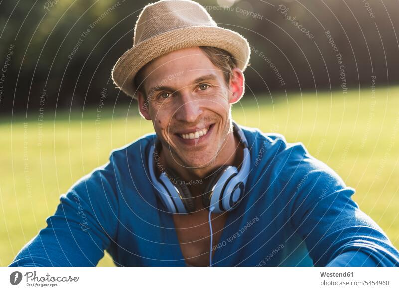 Porträt eines lachenden Mannes mit Hut und Kopfhörer in einem Park Portrait Porträts Portraits Hüte Männer männlich Erwachsener erwachsen Mensch Menschen Leute
