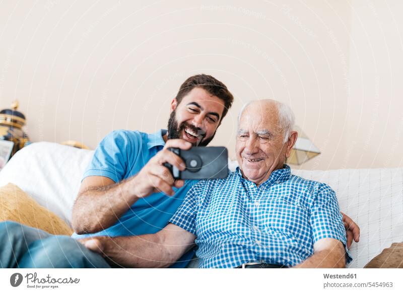 Porträt eines erwachsenen Enkels und seines Großvaters, die zu Hause ein Selfie mit dem Smartphone machen Selfies Enkelsöhne Enkelsohn Senior ältere Männer