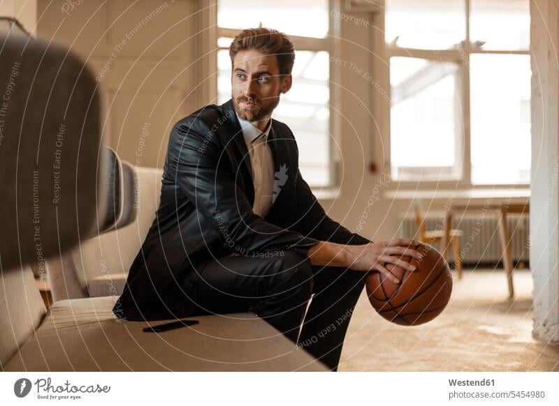 Porträt eines jungen Geschäftsmannes mit Basketball, der auf der Couch in einem Loft sitzt Mann Männer männlich Businessmann Businessmänner Geschäftsmänner