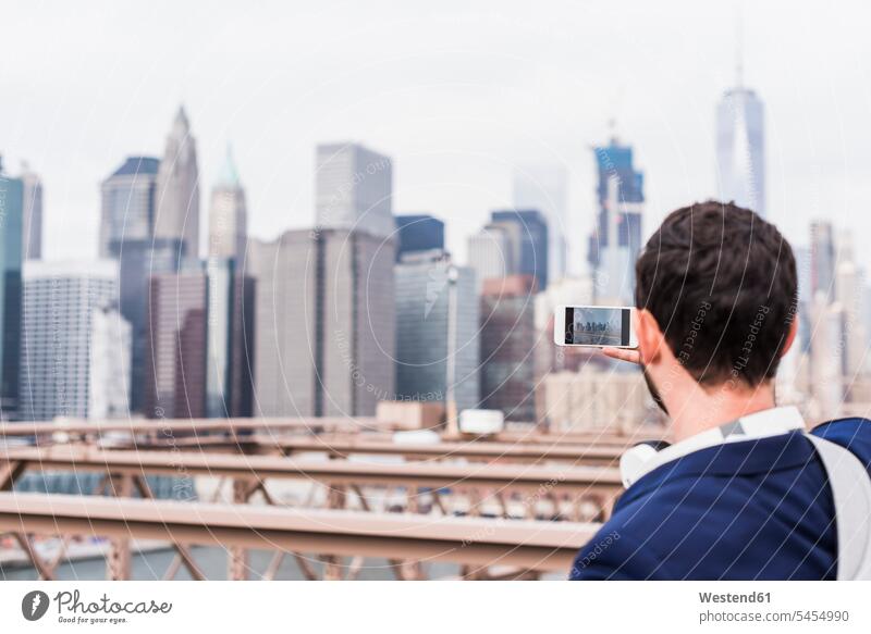 USA, New York City, Mann auf der Brooklyn Bridge beim Fotografieren mit dem Handy fotografieren Mobiltelefon Handies Handys Mobiltelefone Männer männlich