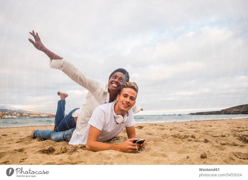 Glückliches junges Paar am Strand Pärchen Paare Partnerschaft Beach Straende Strände Beaches Mensch Menschen Leute People Personen Meer Meere liegen liegend