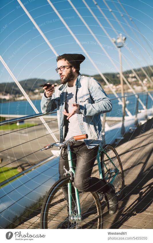 Junger Mann mit Fixie-Rad auf einer Brücke mit Smartphone Fahrrad Bikes Fahrräder Räder telefonieren anrufen Anruf telephonieren Handy Mobiltelefon Handies