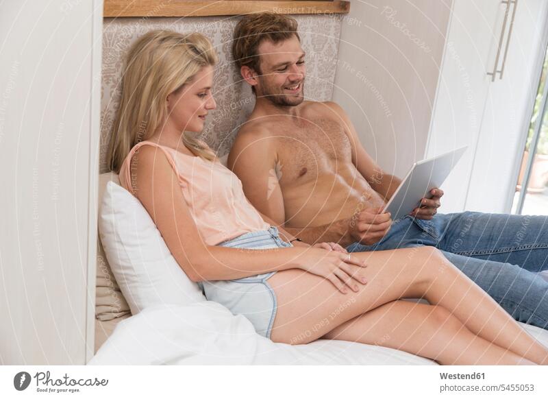 Lächelndes junges Paar mit Tablette im Schlafzimmer Bett Betten lächeln Tablet Computer Tablet-PC Tablet PC iPad Tablet-Computer Pärchen Paare Partnerschaft
