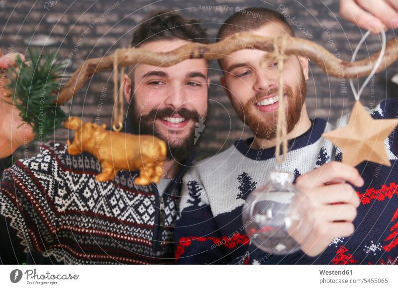 Schwules Paar schmückt einen Zweig zur Weihnachtszeit Schwuler schmücken geschmueckt dekorieren dekoriert geschmückt schmuecken Gleichgeschlechtliches Paar