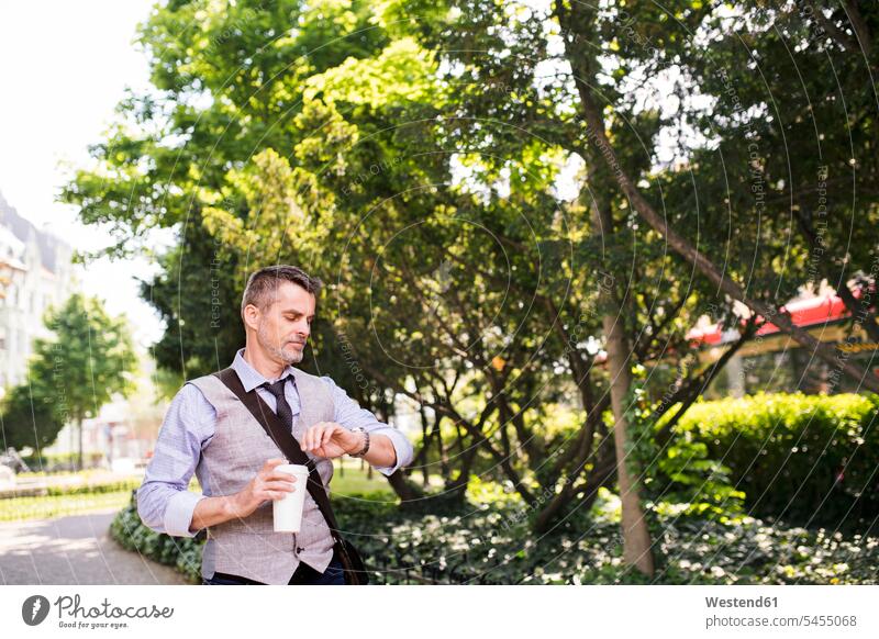 Reifer Geschäftsmann mit Kaffee im Stadtpark bei der Zeitkontrolle Armbanduhr Armbanduhren Mann Männer männlich Getränk Getraenk Getränke Getraenke