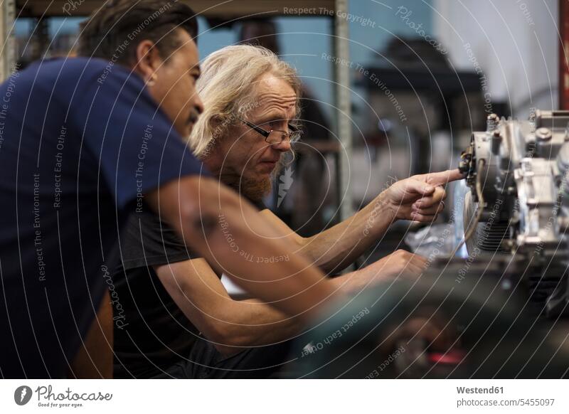 Zwei Mechaniker arbeiten in der Werkstatt am Motorradmotor reparieren Reparatur Arbeit Monteur Motorräder Kollegen Arbeitskollegen Industrie industriell Gewerbe