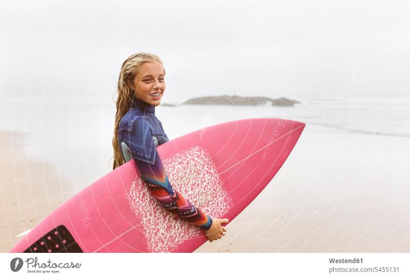 Spanien, Aviles, junger Surfer mit Surfbrett am Strand lächeln Surfbretter surfboard surfboards Surferin Wellenreiterinnen Surferinnen Meer Meere Beach Straende
