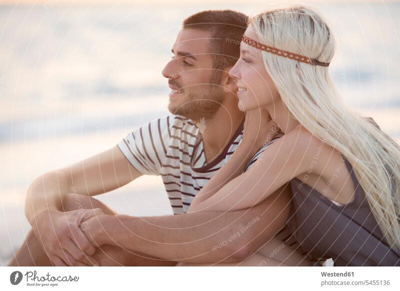 Junges Paar sitzt am Strand und umarmt Meer Meere Beach Straende Strände Beaches sitzen sitzend romantisch schwärmerisch schwaermerisch gefuehlvoll gefühlvoll