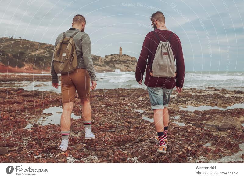 Spanien, Oropesa del Mar, zwei junge Männer gehen am steinigen Strand spazieren Beach Straende Strände Beaches Paar Pärchen Paare Partnerschaft Mensch Menschen