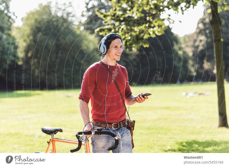 Lachender Mann mit Rennrad, der in einem Park mit Kopfhörern Musik hört Männer männlich Parkanlagen Parks Erwachsener erwachsen Mensch Menschen Leute People