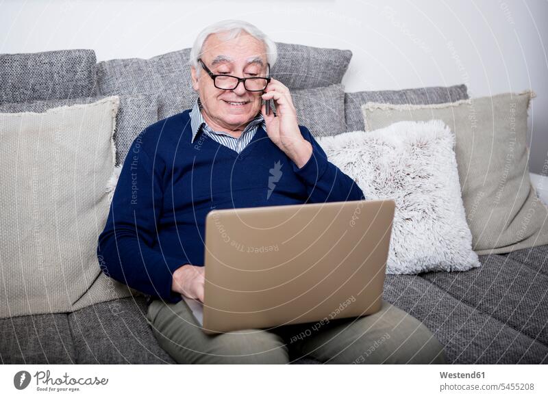 Älterer Mann sitzt auf der Couch und benutzt Laptop und Smartphone Sofa Couches Liege Sofas Senior ältere Männer älterer Mann Senioren telefonieren anrufen