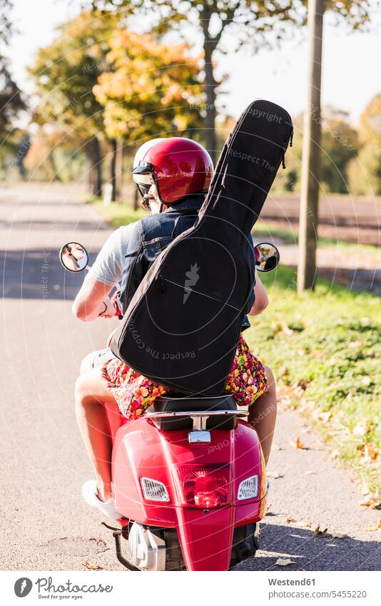Junges Paar fährt Motorroller mit Gitarrentasche auf dem Rücken Tasche Taschen Roller Piaggio Pärchen Paare Partnerschaft fahren Kraftfahrzeug Verkehrsmittel