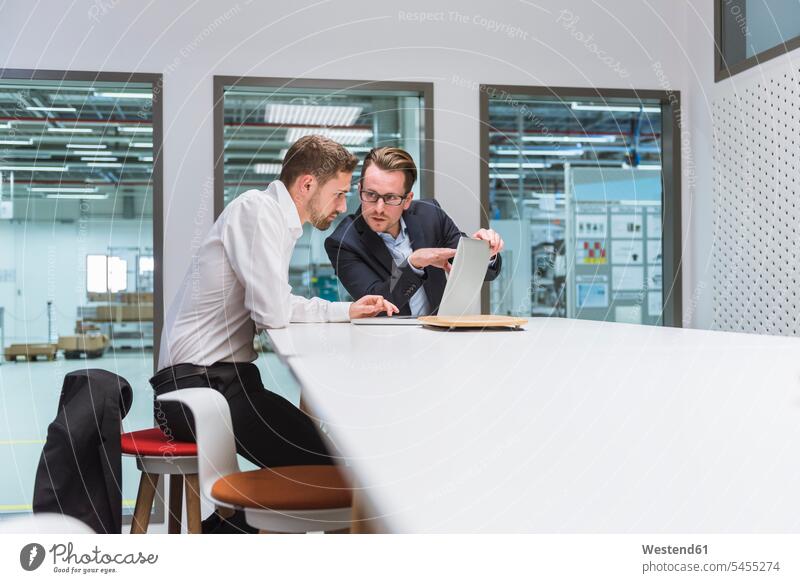 Zwei Geschäftsleute sitzen in einem modernen Büro und diskutieren vor einem Laptop Kollegen Arbeitskollegen Team Geschäftsmann Businessmann Businessmänner