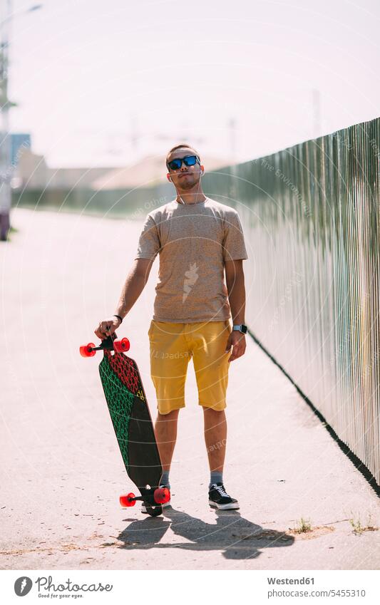 Porträt eines selbstbewussten jungen Mannes mit Longboard Skateboard Rollbretter Skateboards stehen stehend steht Männer männlich Erwachsener erwachsen Mensch