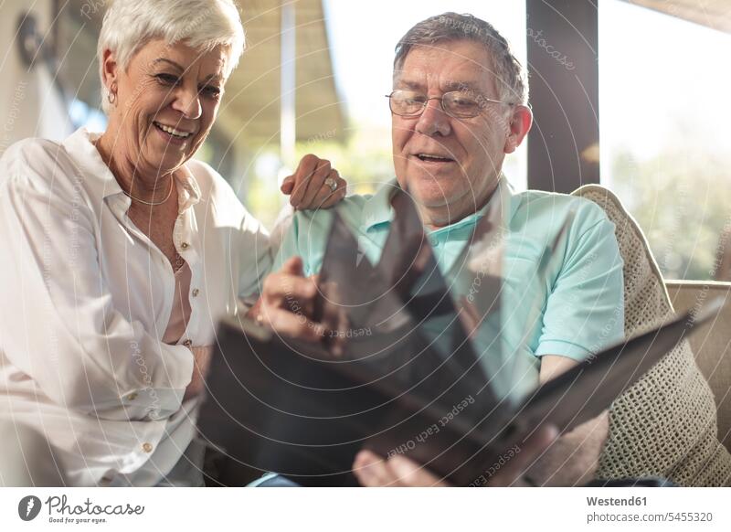 Glückliches älteres Paar sitzt auf der Couch und schaut sich ein Fotoalbum an Sofa Couches Liege Sofas ansehen glücklich glücklich sein glücklichsein Zuhause