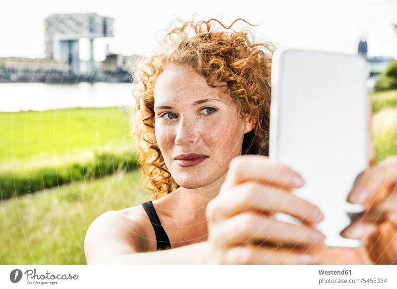 Deutschland, Köln, Porträt einer sommersprossigen jungen Frau, die ein Selfie mit ihrem Handy macht Portrait Porträts Portraits weiblich Frauen Selfies