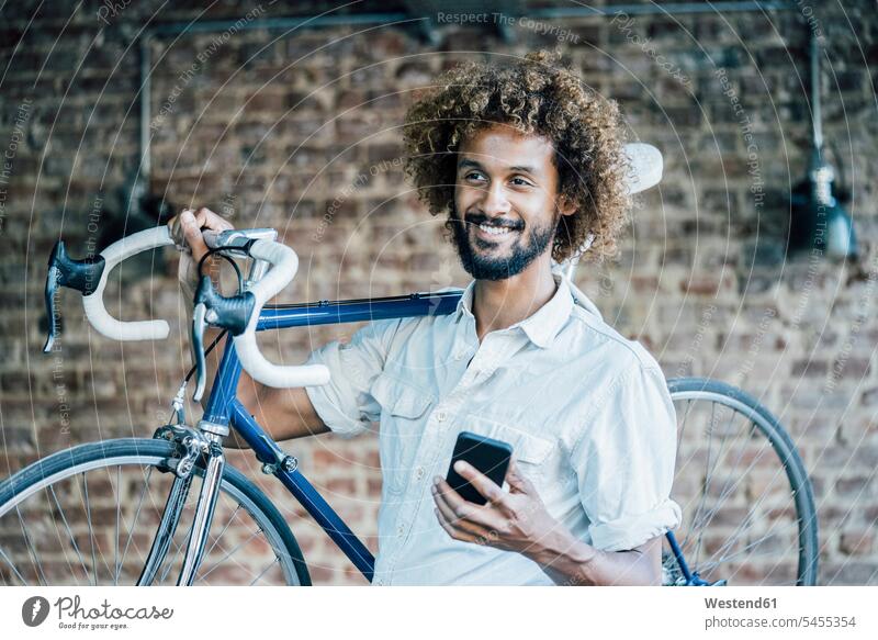 Lächelnder junger Mann mit Fahrrad und Handy Bikes Fahrräder Räder Rad lächeln Männer männlich Mobiltelefon Handies Handys Mobiltelefone Raeder Erwachsener
