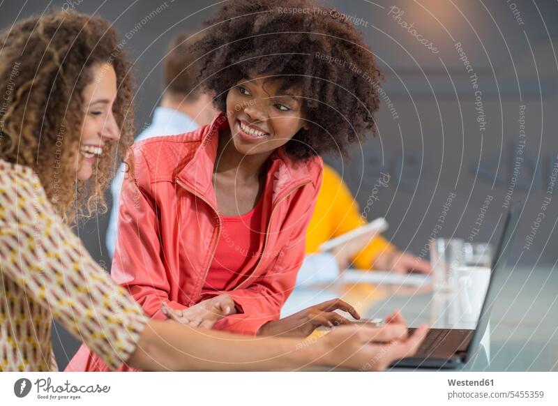 Zwei glückliche Frauen im Büro teilen sich einen Laptop Office Büros lächeln Notebook Laptops Notebooks Kollegin Kolleginnen lachen Arbeitsplatz Arbeitsstätte