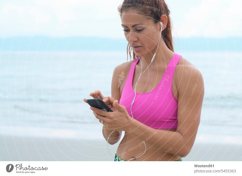 Frau hört Musik von ihrem Smartphone Musik hören iPhone Smartphones fit Strand Beach Straende Strände Beaches sportlich weiblich Frauen Handy Mobiltelefon