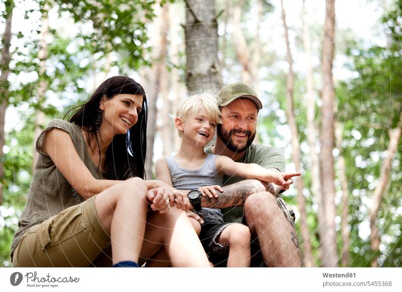 Glückliche Familie mit Sohn im Wald sitzend lachen zeigen mit dem Finger zeigen deuten Familien Forst Wälder Söhne positiv Emotion Gefühl Empfindung Emotionen