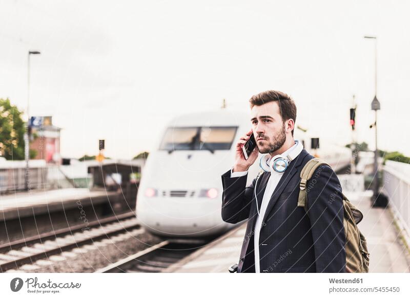 Junger Mann benutzt Mobiltelefon auf dem Bahnsteig als einfahrender Zug reisen Travel verreisen Weg Reise telefonieren anrufen Anruf telephonieren Männer