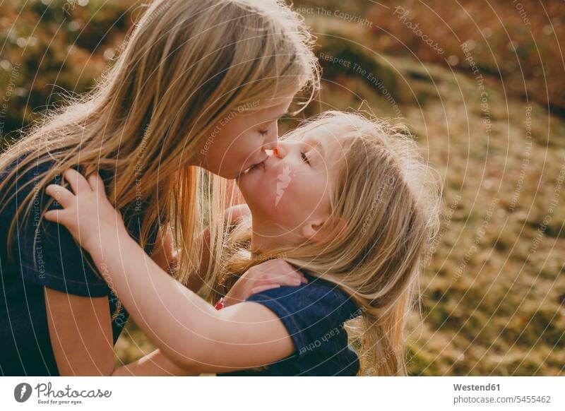 Zwei süße blonde Schwestern küssen sich im Freien Küsse Kuss umarmen Umarmung Umarmungen Arm umlegen Mädchen weiblich Geschwister Familie Familien Mensch
