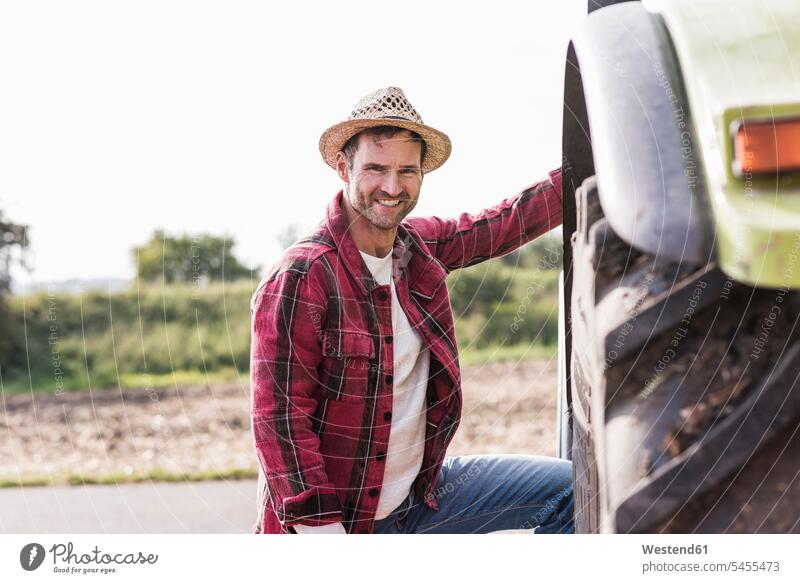 Porträt eines selbstbewussten Landwirts mit Traktor Portrait Porträts Portraits Schlepper Traktoren Trecker Mann Männer männlich Bauer Landwirte Bauern lächeln