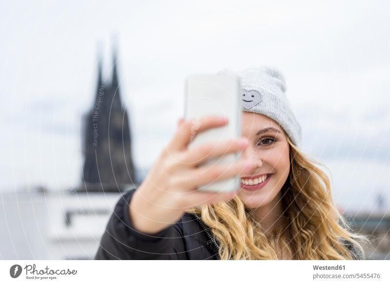 Deutschland, Köln, Porträt einer lachenden jungen Frau, die ein Selfie mit ihrem Smartphone macht iPhone Smartphones Portrait Porträts Portraits Selfies