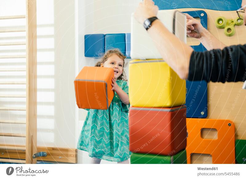 Glückliches kleines Mädchen hebt einen weichen Baustein im Turnsaal eines Kindergartens hoch Kids spielen weiblich Kindergaerten Kindergärten Mensch Menschen