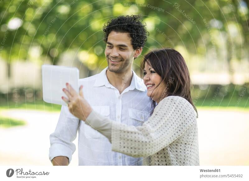 Lächelnde Mutter und erwachsener Sohn schauen Tablette im Park an Tablet Computer Tablet-PC Tablet PC iPad Tablet-Computer Mami Mutti Mütter Mama lächeln